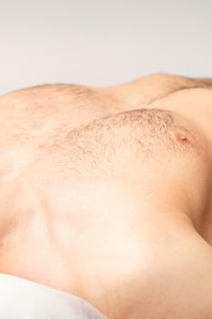 Hairy body, stomach, and chest of a man lying before epilation