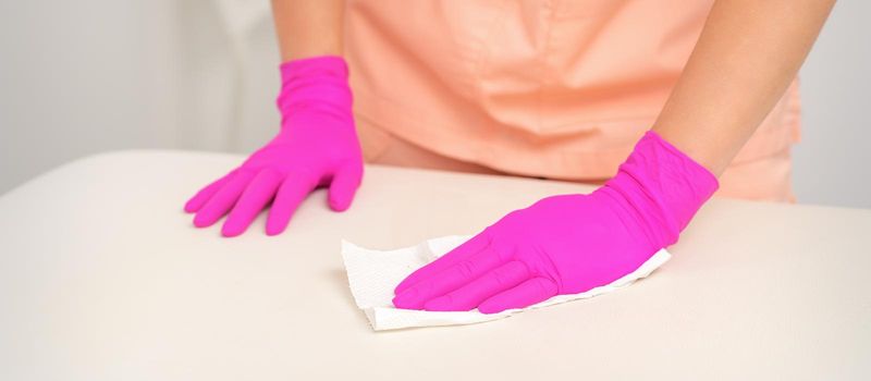 Close up of hands in rubber protective pink gloves cleaning the white surface with a white rag