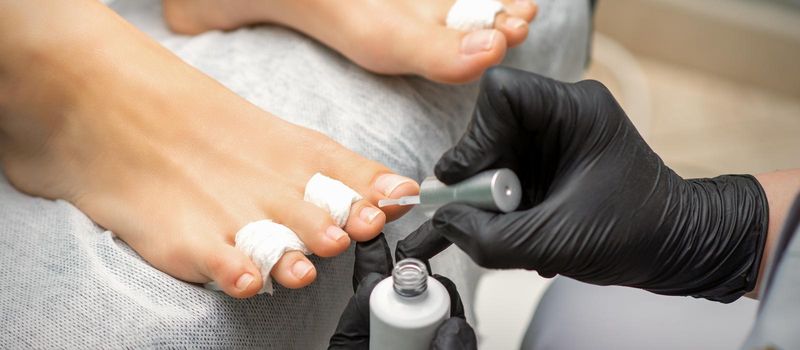 Pedicurist applying transparent varnish to the female toenails in a beauty salon