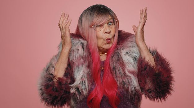 What Why. Sincere irritated elderly woman raising hands in indignant expression asking reason of failure demonstrating disbelief irritation by troubles. Senior confused grandmother on pink background