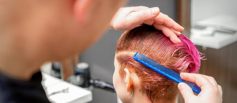 Combing the hair of a young woman during coloring hair in pink color at a hair salon close up