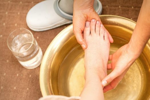 Washing female foot in a special container by male masseur in spa salon