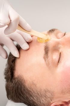 Beautician applying wax paste between eyebrows during the procedure of waxing in the beauty salon