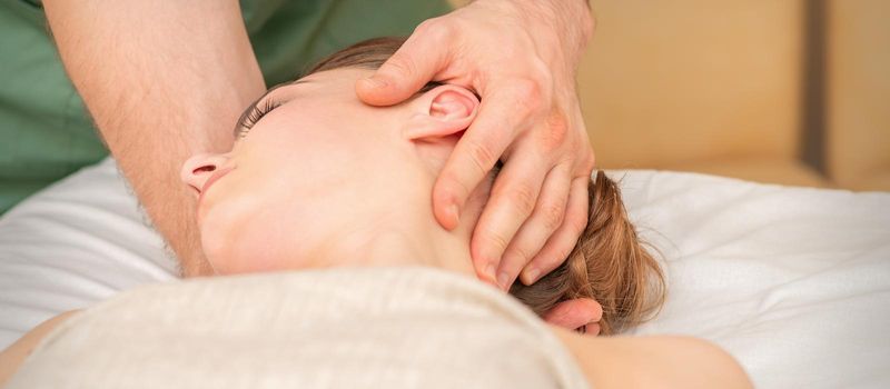 Osteopath doing massage on the female head in rehabilitation clinic center