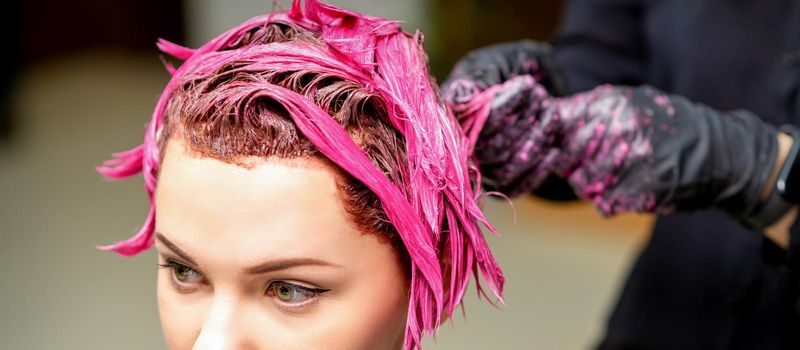 The professional hairdresser uses a brush to apply the pink dye to the hair. Hair coloring concept