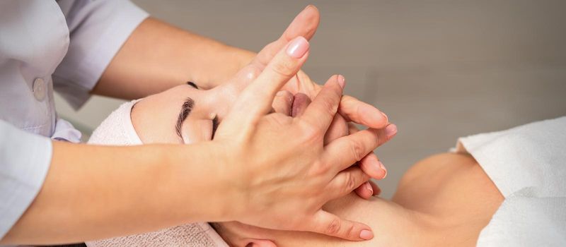 Beautiful caucasian young woman getting a facial massage at a beauty salon