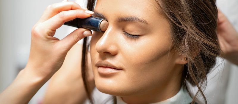 Make up artist contouring the face of a young woman with cream blush close up