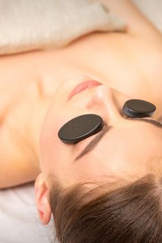 Massage with stones on the eyes of young woman getting a treatment in a beauty spa