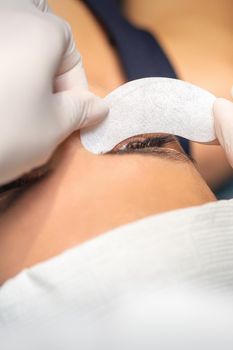 The beautician is gluing a patch under her eyes, before the procedure of eyelash extension. Artificial extended eyelashes