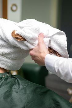 A hairdresser is wrapping the wet hair of the young woman in a towel after washing at the beauty salon