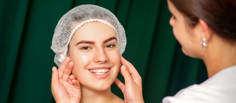 Doctor examining the beautiful face of young smiling woman in beauty clinic