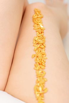 Sugaring concept. Wax granules lying in a row on female legs close up