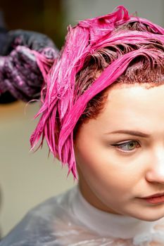 The professional hairdresser uses a brush to apply the pink dye to the hair. Hair coloring concept