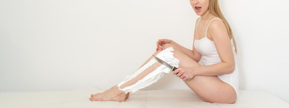 Beautiful caucasian woman shaving her legs with a knife with shaving foam on white background. Depilation and epilation concept