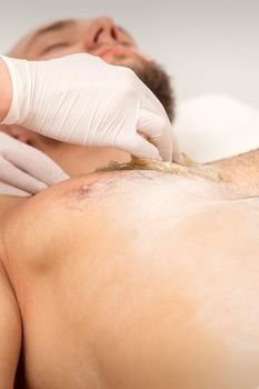 Epilation chest of a young male with the liquid wax paste in a beauty salon