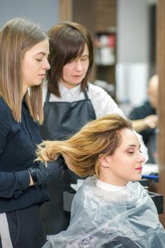 Two female hairstylists prepare long hair of a young woman making curls hairstyle in a beauty salon