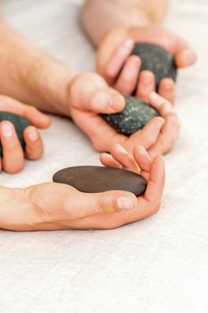 Four hands of male masseurs holding spa stones on white towel top view. Stone massage concept