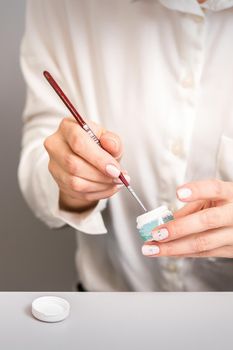 Blue glitter nail polish with a nail brush in hands of female manicurist