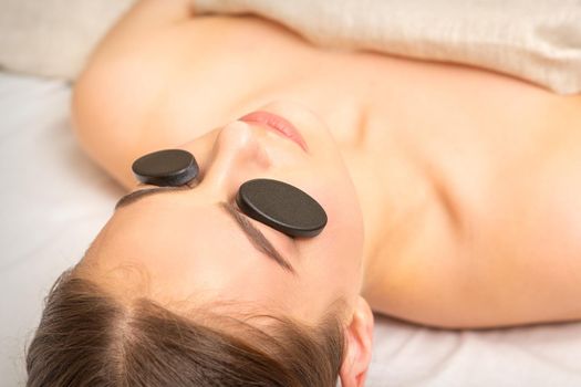 Massage with stones on the eyes of young woman getting a treatment in a beauty spa