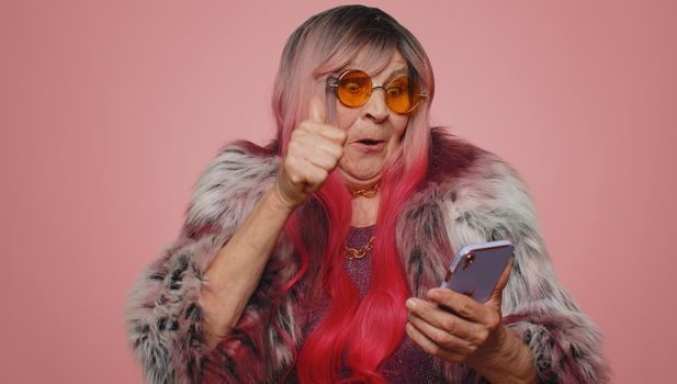 Happy excited joyful old woman grandmother in coat use mobile cell phone typing browsing shouting say wow yes found out great big win, good news, lottery goal achievemen, celebrating success, winning