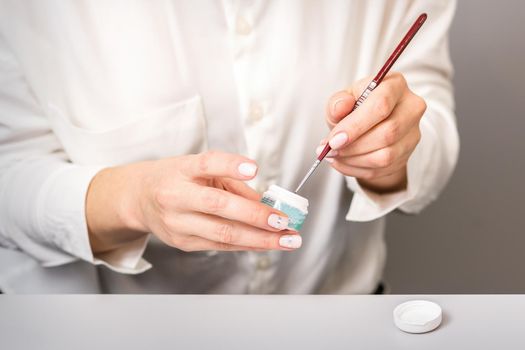 Blue glitter nail polish with a nail brush in hands of female manicurist