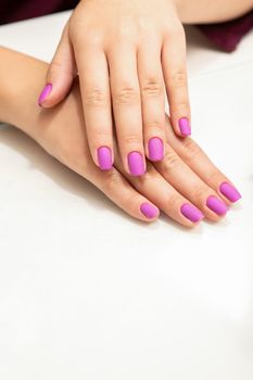 Beautiful fingers with purple nails after nail polish procedure in manicure salon