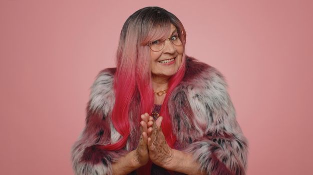 Sneaky cunning woman with tricky face gesticulating and scheming evil plan, thinking over devious villain idea, cunning cheats, jokes and pranks. Senior grandmother on pink studio background indoors