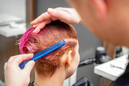 Combing the hair of a young woman during coloring hair in pink color at a hair salon close up