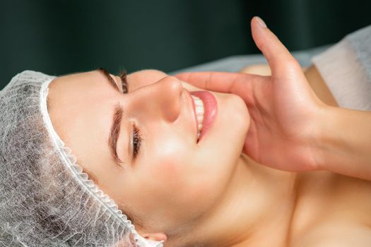 Doctor examining the beautiful face of young smiling woman in beauty clinic