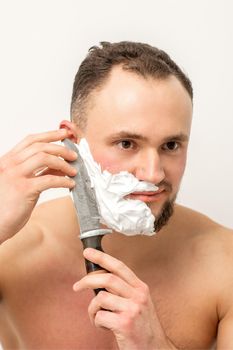 Young caucasian man shaving beard with a big knife on white background