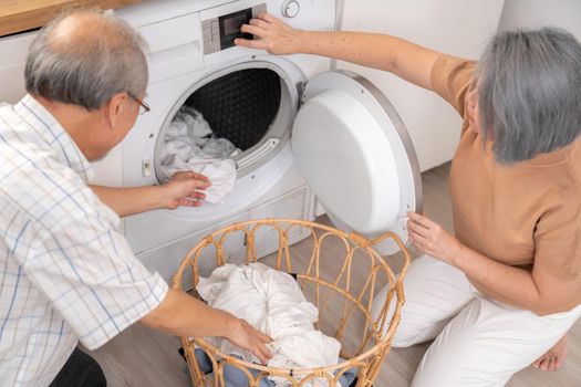 Senior couple working together to complete their household chores at the washing machine in a happy and contented manner. Husband and wife doing the usual tasks in the house.
