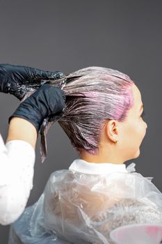 A hairdresser is applying color to the hair of a customer. Hair coloring in a beauty salon. Beauty and people concept. Close-up back view