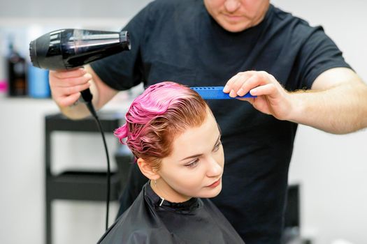 A hairdresser is drying the pink hair of the young woman in a beauty salon