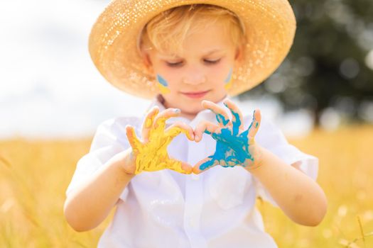 Stop War in Ukraine. Love Ukraine concept. Ukrainian boy with Ukrainina flag- yellow and blue painted on the hands forming a heart stands against war.