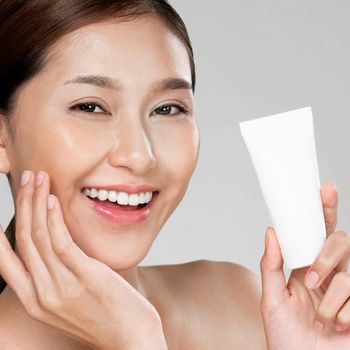 Closeup ardent woman smiling holding mockup product for advertising text place, light grey background. Concept of healthcare for skin, beauty care product for advertising.