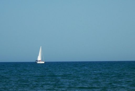 Sailboat in the blue sea with blue sky in the background