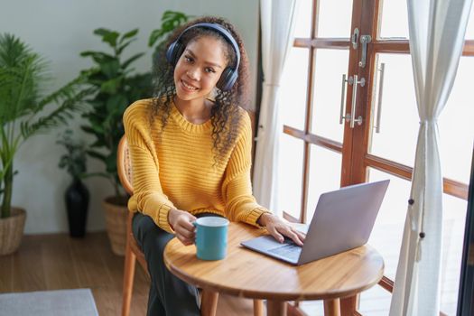 Portrait of an African American wearing headphones holding a coffee cup and using a computer.