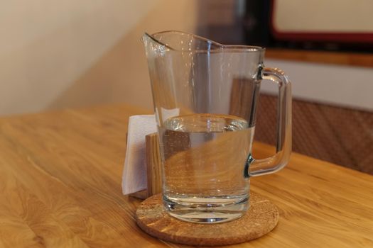 A decanter with drinking water on a wooden table. Interior of a cozy coffee shop. White paper napkins. Glass transparent decanter.