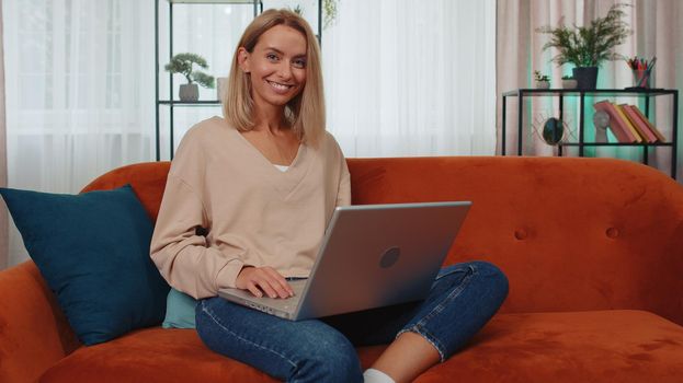 Portrait of girl freelancer at home room sits on couch, opens laptop. Young business woman start remote work on notebook, sends messages, makes online purchases, watching movies, distance education