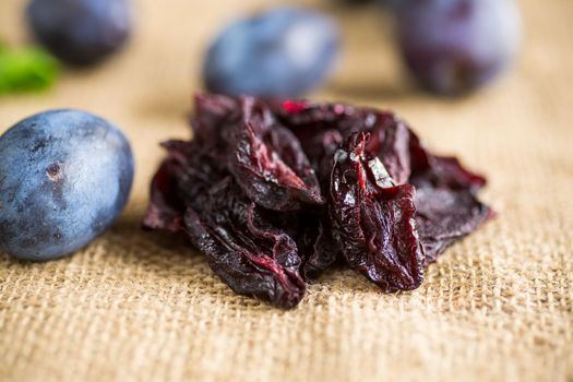 Dried prunes in a spoon on a burlap tablecloth against a background of fresh plums. Prunes and plums on a kitchen table close-up.