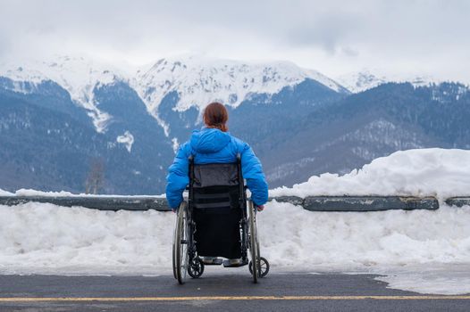 Rear view of a woman in a wheelchair travels in the mountains in winter