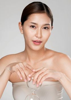 The concept of anti-aging demonstrated by closeup portrait of an ardent young woman holding an hourglass. Skincare treatment, beauty care and cosmetic ideas.