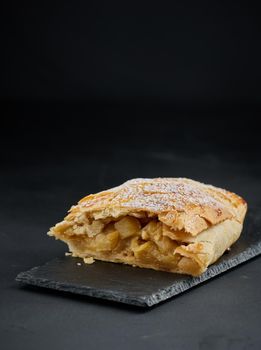 Baked strudel with apples sprinkled with powdered sugar on a black board, delicious dessert