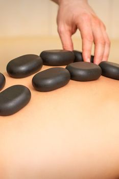 Young caucasian woman receiving back massage with black stones by masseur in spa salon. A woman getting a spa treatment