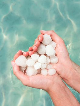 Hands holding sea salt crystals heart-saped on sea water background. Dead sea salt spa minerals cosmetic concept