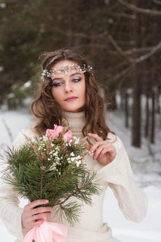 Beautiful bride in a white dress with a bouquet in a snow-covered winter forest. Portrait of the bride in nature.