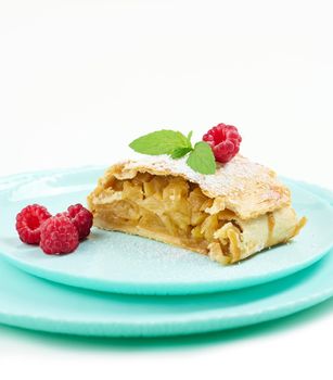 Slice of apple strudel on a round plate, white background