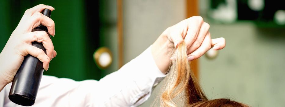 Female coiffeur fixing hairstyling of blonde woman with hairspray in a beauty salon