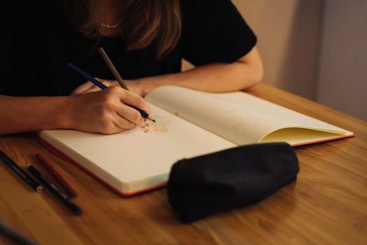 A girl in a cafe draws in a sketchbook with colored pencils. Notepad, pencils, black pencil case.