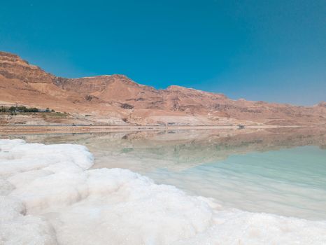 Landscape view on Dead Sea salt crystals formations, clear cyan green calm water and mountains at Ein Bokek beach, Israel